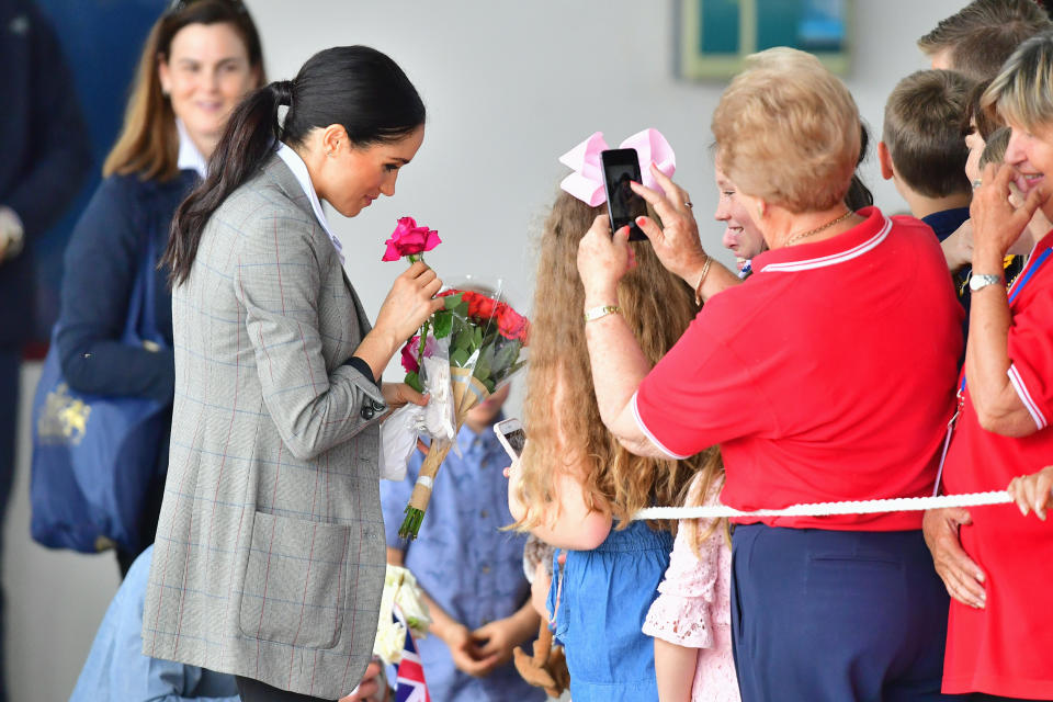 Meghan takes a moment to appreciate some flowers given to her. Photo: Getty, meghan markle prince harry dubbo, meghan markle prince harry australia, meghan markle serena williams jacket, meghan markle pregnant