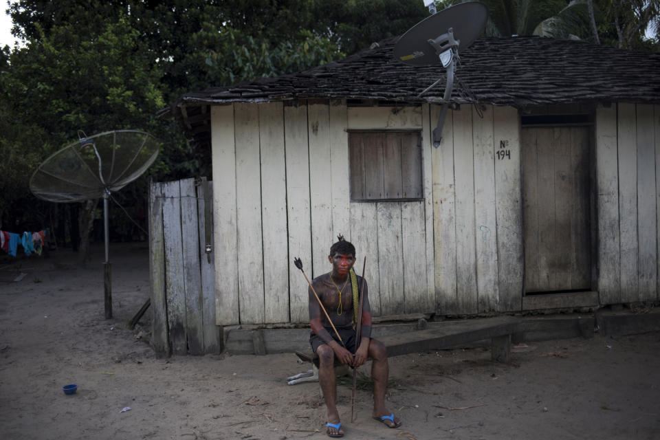 In this Sept. 3, 2019 photo, a man sits outside his wooden home on a break from a meeting of Tembé tribes at the Tekohaw indigenous reserve, Para state, Brazil. bout 600 members of the tribe live in Tekohaw. It’s located on the banks of the Gurupi River where many fish for piranhas and other fish that they later grill over wood fires. Deep in the jungle, armed with spears and arrows, they hunt for birds, pigs and other animals. (AP Photo/Rodrigo Abd)