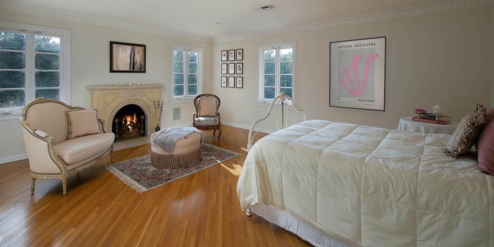 a bedroom with a bed by two armchairs and a fireplace