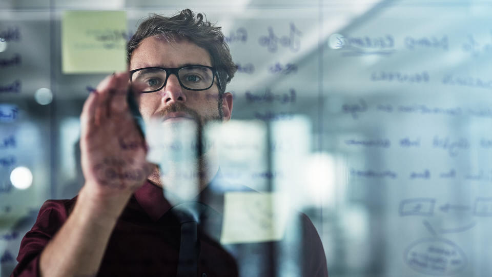 Shot of a young businessman brainstorming with sticky notes on a glass wall in a modern office.