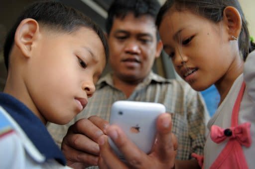 File illustration photo shows a man look at his mobile phone with his children in Phnom Penh. Children must be taught to reflect before hitting the "send" button on something they might later regret, refrain from anonymous comments, and not to believe everything they read or see online