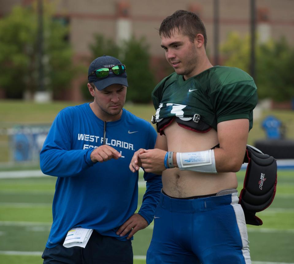 University of West Florida coach Kaleb Nobles checks on quarterback Mike Beaudry’s hand at the close of practice on Friday, Aug. 10, 2018.
