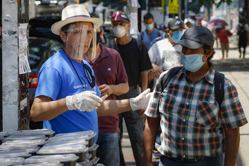 Walther Sinche directs pedestrians toward food donations during the COVID-19 pandemic, Tuesday, June 23, 2020, in the Corona neighborhood of the Queens borough of New York. (AP Photo/John Minchillo)