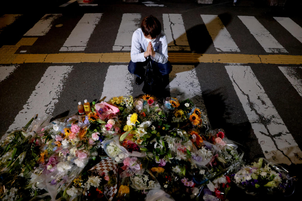 A person prays next to dozens of bouquets laid on the street.