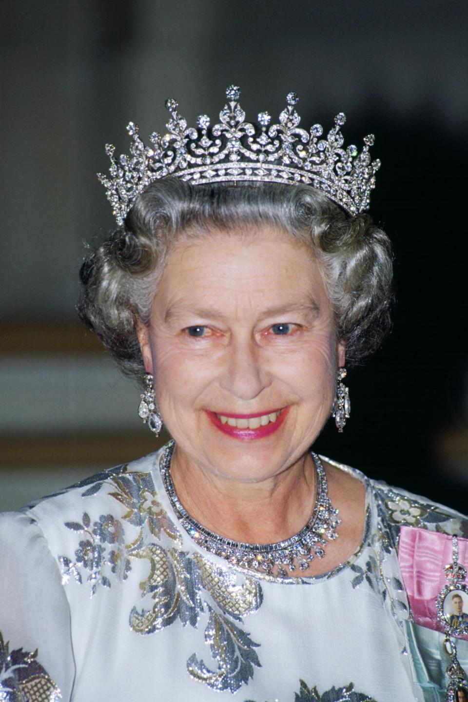 FRANCE - JUNE 10: Queen Elizabeth II attends a banquet in Paris wearing a white evening dress embroidered with silver by designer Ian Thomas, the Queen Mary's Girls of Great Britain and Ireland tiara and a the King Faisal of Saudi Arabia necklace (Photo by Tim Graham Photo Library via Getty Images)