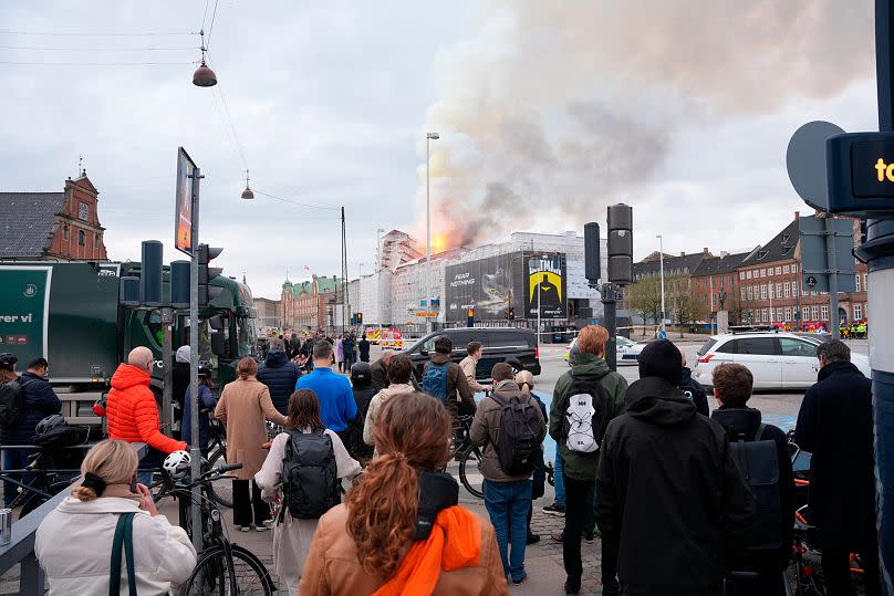 People watch as fire and smoke rise out of the Old Stock Exchange, Boersen, in Copenhagen, Denmark, Tuesday, April 16, 2024.