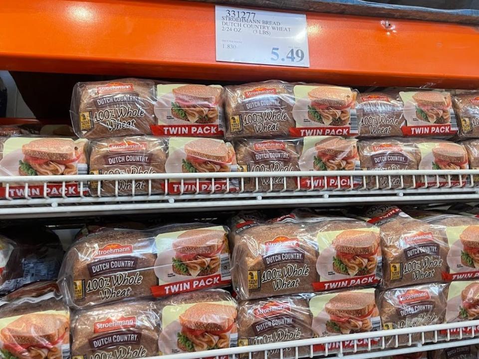 Twin packs of 100% whole wheat bread on shelves at Costco, with a price tag that reads $5.49.