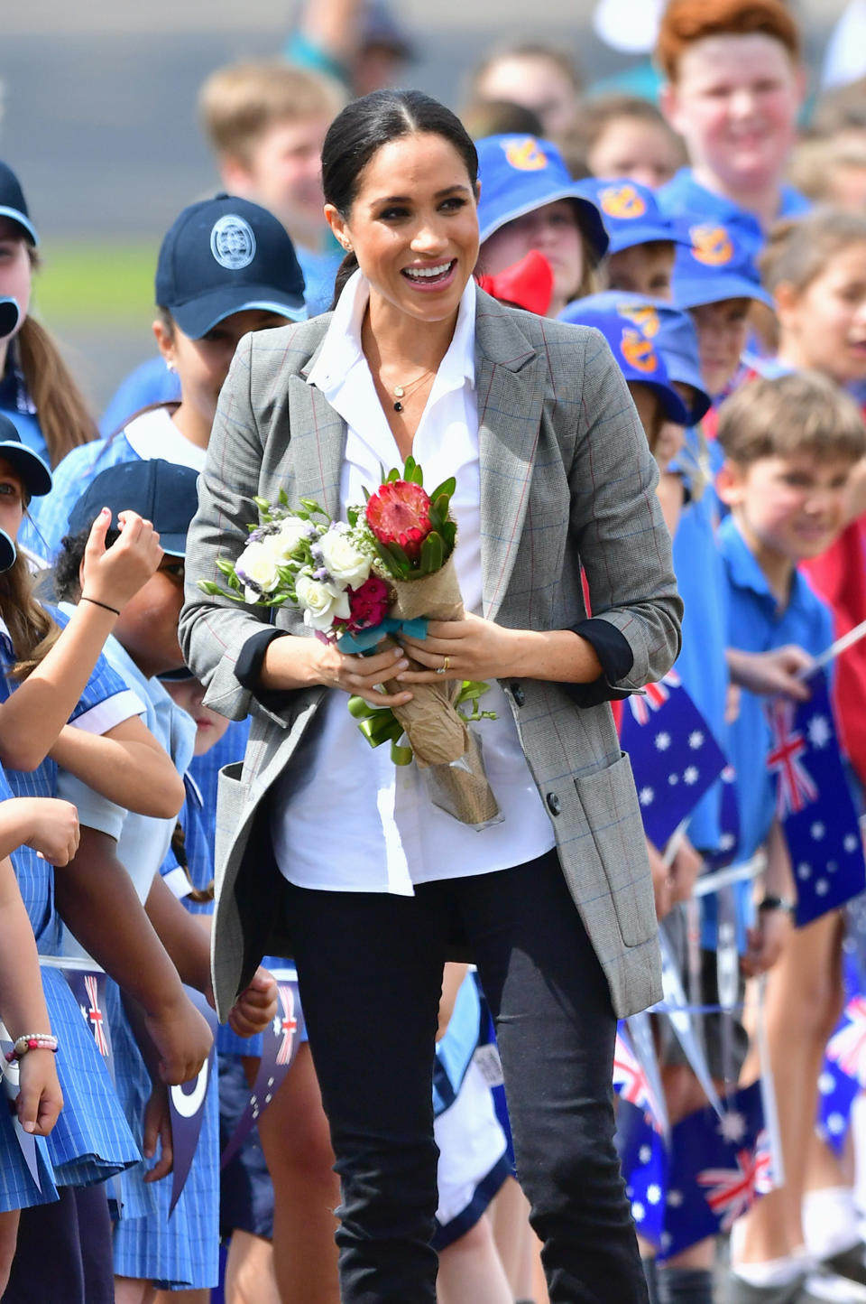 Meghan with a bunch of beautiful flowers given to her upon arrival in Dubbo. Photo: Getty, meghan markle prince harry dubbo, meghan markle prince harry australia, meghan markle serena williams jacket, meghan markle pregnant