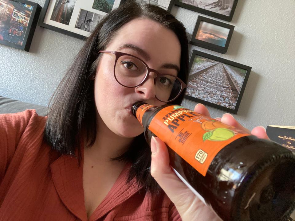 Paige in a red shirt drinking aldi sparkling apple cider out of bottle