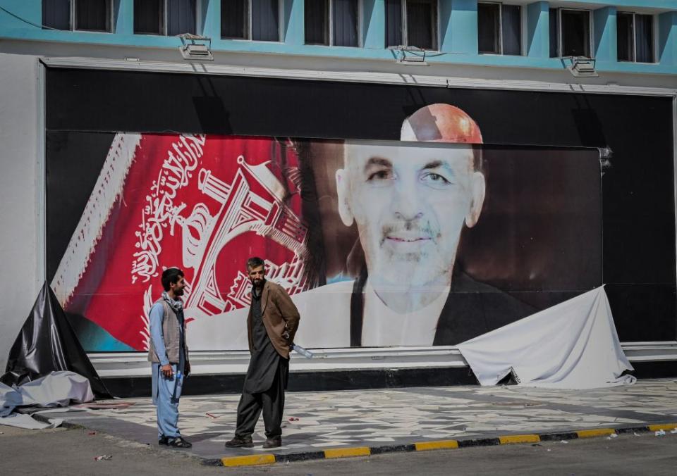 Afghan men stand next to the a torn poster of Afghan President Ashraf Ghani at the Kabul airport in Kabul.