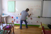 Manuel, director de una escuela, escribe un mensaje de bienvenida en la pizarra de una clase en el colegio de primaria Isabel la Católica en Madrid, España, el lunes 31 de agosto de 2020. Algunos padres españoles se resisten a enviar de vuelta a la escuela a sus hijos, en medio de un auge de los contagios de coronavirus. (AP Foto/Andrea Comas)