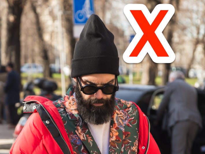red x next to a man wearing a black oversized beanie, a floral suit, and a red puffer jacket looking at his phone while walking down a sidewalk