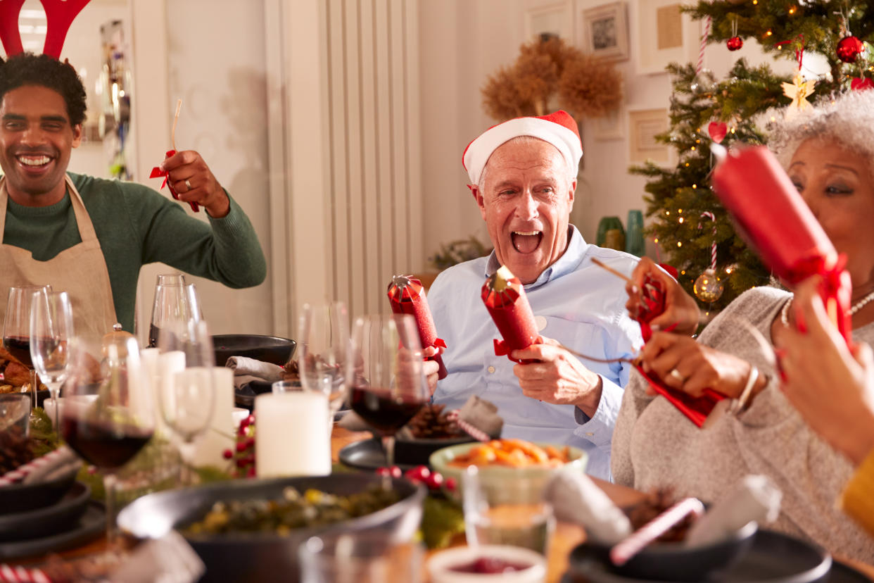 Multi Generation Family Pulling Christmas Crackers As They Sit For Meal At Table