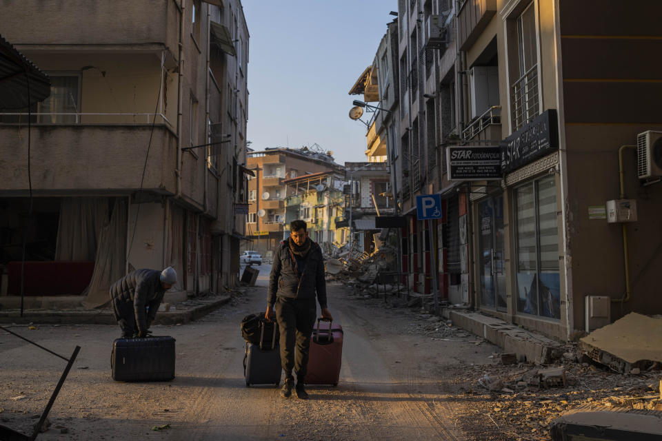 Two men carry belongings as they leave a neighbourhood heavily affected by an earthquake in Antakya, southeastern Turkey, Monday, Feb. 13, 2023. Thousands left homeless by a massive earthquake that struck Turkey and Syria a week ago packed into crowded tents or lined up in the streets Monday for hot meals as the desperate search for survivors entered what was likely its last hours. (AP Photo/Bernat Armangue)