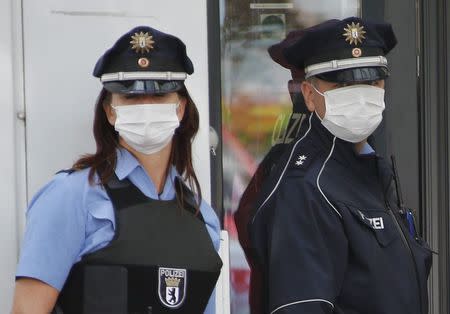 Police officers wearing protective masks stand outside the entrance of a job centre in the Berlin district of Pankow August 19, 2014. REUTERS/Fabrizio Bensch