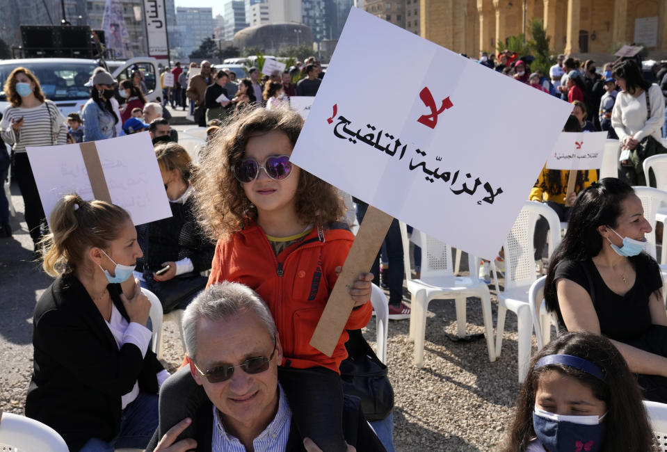 A protester carries her daughter on his shoulders who holds an Arabic placard that reads:"No for mandatory vaccination," during a rally to protest measures imposed against people who are not vaccinated, in Beirut, Lebanon, Saturday, Jan. 8, 2022. Vaccinations are not compulsory in Lebanon but in recent days authorities have become more strict in dealing with people who are not inoculated or don't carry a negative PCR test. (AP Photo/Hussein Malla)
