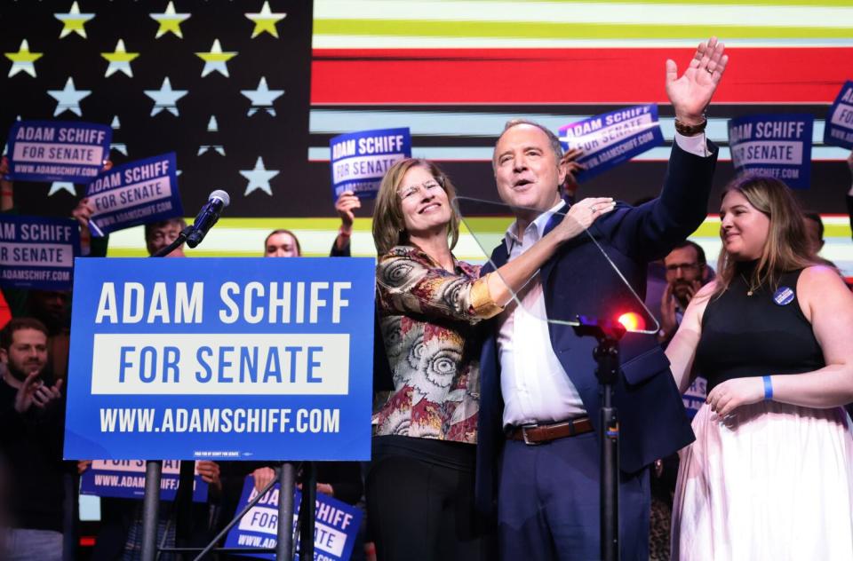 A woman has her hand on the shoulder of a man in a dark jacket, with one hand raised in celebration.