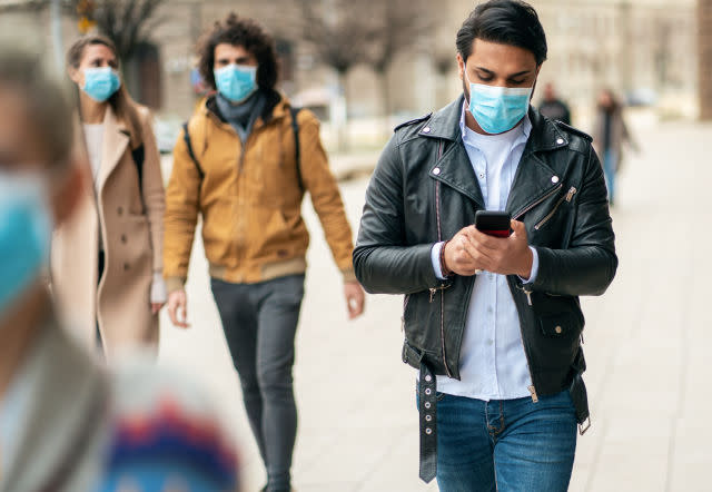 Portrait of young man on the street wearing face protective mask to prevent Coronavirus and anti-smog and using smartphone