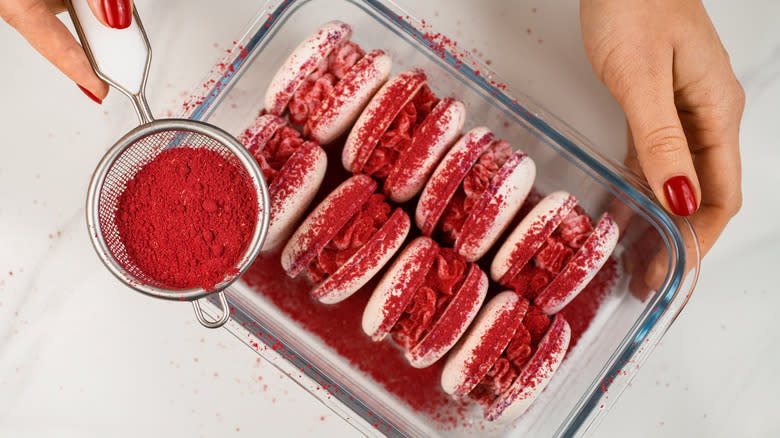 Sprinkling red powder over macarons