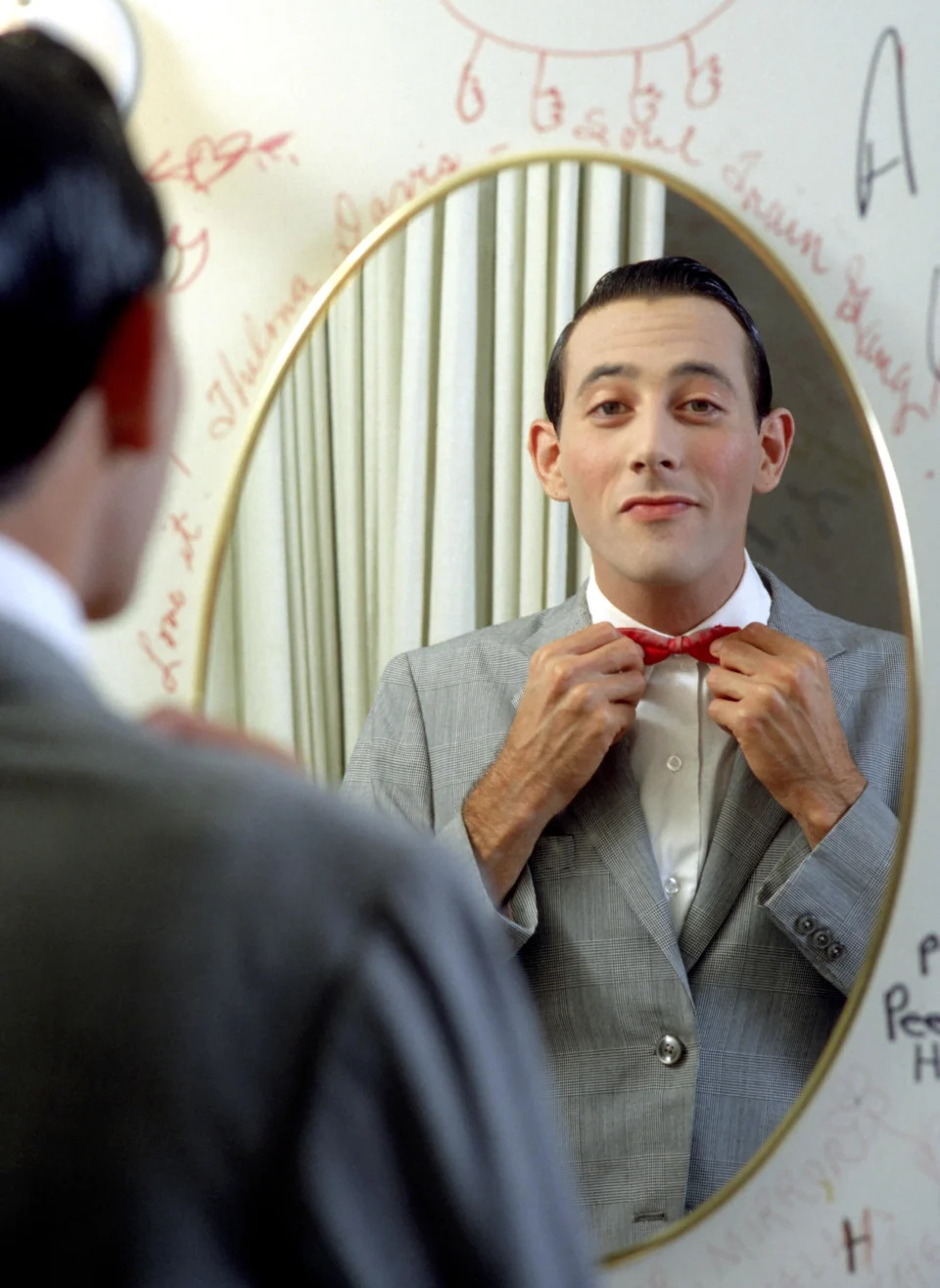 Paul Reubens looks at the camera through the reflection of a mirror as character Pee-wee Herman.