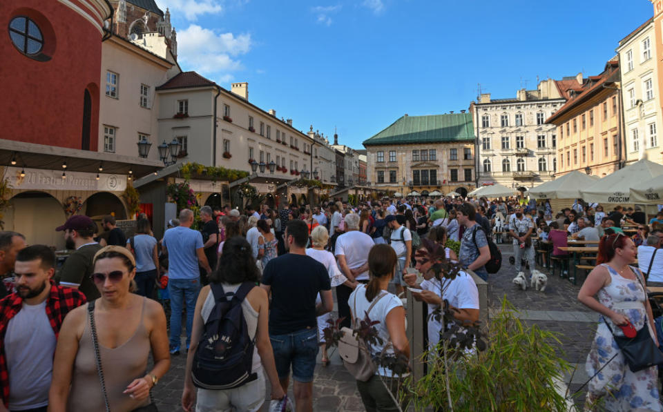 A bustling town square filled with people enjoying an outdoor market, with buildings in the background under a clear sky