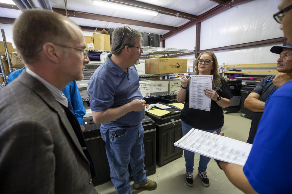Torrance County deputy clerk Silvia Chavez, center, shows a ballot sample to local candidates and partisan officers during a ballot-counting machines testing in Estancia, N.M., Sept. 29, 2022. (AP Photo/Andres Leighton)