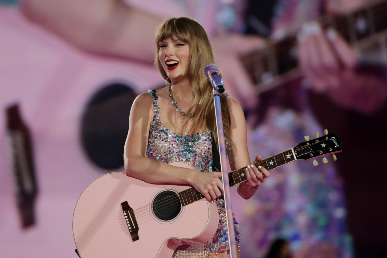 Taylor Swift, holding a guitar, performs onstage.