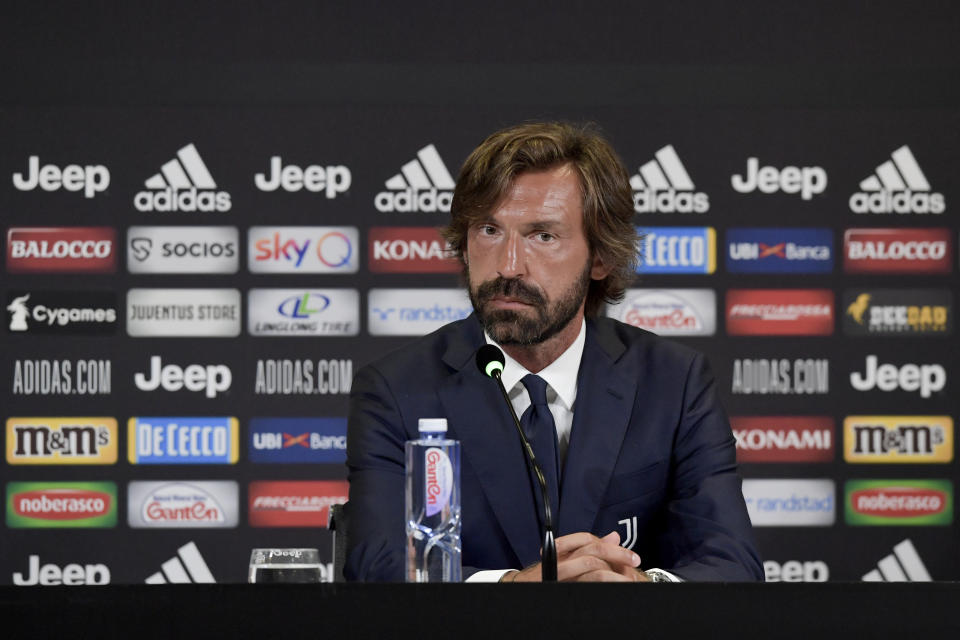 Andrea Pirlo sits in front of a microphone at a podium.