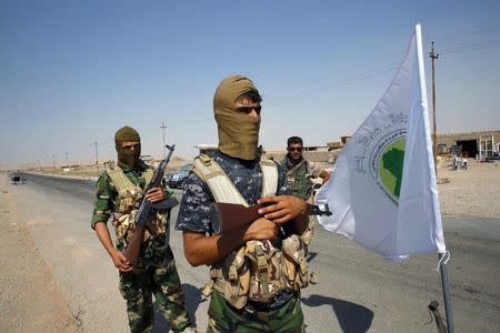 Fighters from the Shi'ite Badr Brigade militia stand near their flag as they guard at a checkpoint along a highway recently taken from militants of the Islamic State, outside the town of Sulaiman Pek in this September 5, 2014 file photo. REUTERS/Ahmed Jadallah/Files