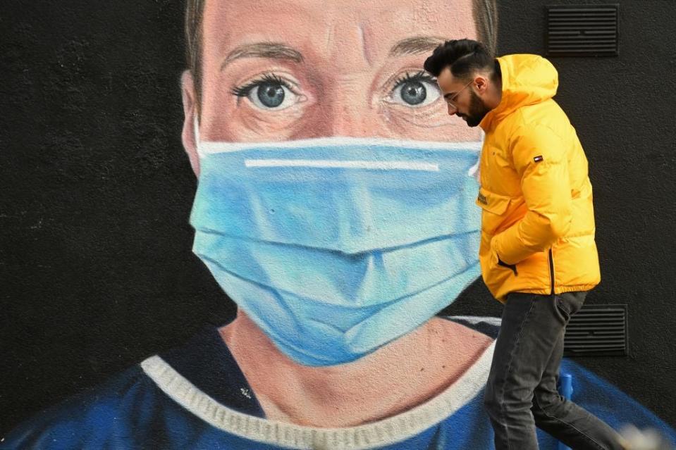 <p>A pedestrian in Manchester walks past graffiti by the artist @akse_p19, depicting an NHS nurse in scrubs and a mask</p> (Getty)