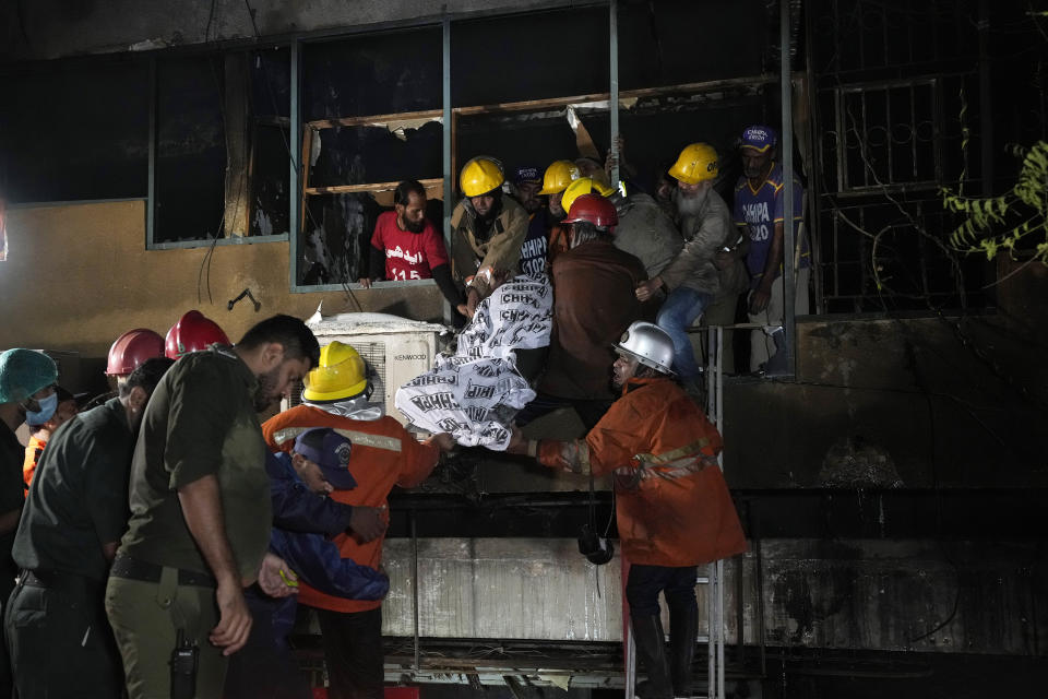 Firefighters and rescue workers recover a body from a burnt multi-story commercial building in Karachi, Pakistan, Wednesday, Dec. 6, 2023. A massive fire broke out Wednesday in a multi-story commercial building in Pakistan's largest southern port city of Karachi, killing a number of people and damaging several shops, police and rescue officials said. (AP Photo/Fareed Khan)