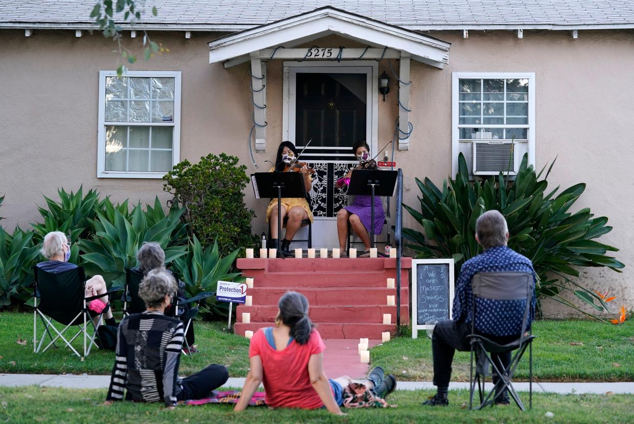 Nancy Kuo, top left, and Manoela Wunder, of the musical duo Masked Strings, perform a concert for their neighborhood on Sunday, Aug. 30, 2020, in the Atwater Village section of Los Angeles, Calif. Kuo and Wunder have been performing as the Masked Strings since May, and perform socially-distanced events in addition to their own concerts since the coronavirus pandemic has prevented them from getting regular music gigs.