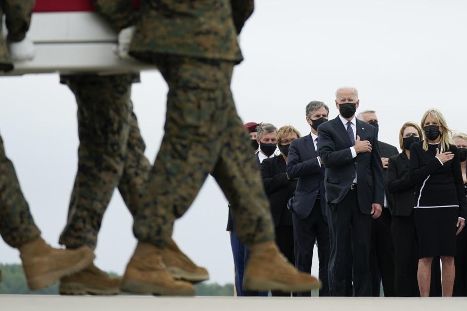President Biden and others watch military personnel carry a coffin