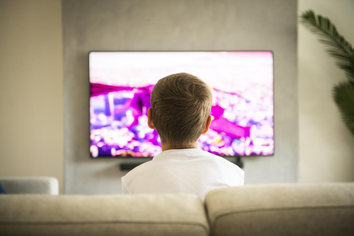 The Back view image of cute boy sitting on sofa and watching TV.�