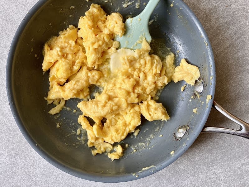 Scrambled eggs in skillet with pad of butter melting and silicone spatula