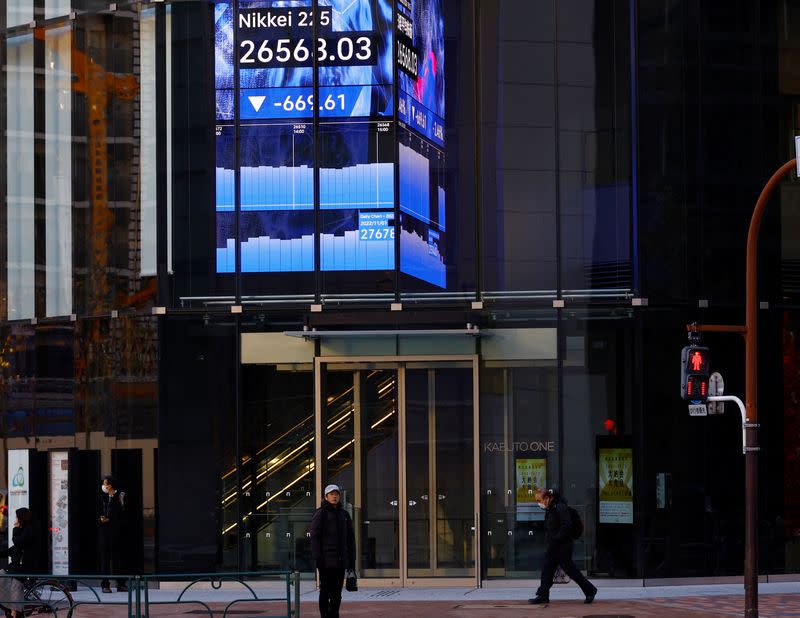 FILE PHOTO: People walk past an electric board showing Nikkei index at a business district in Tokyo