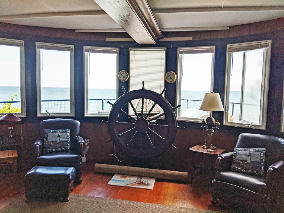 Inside the living room, there is a steering wheel and a view of the lake out several windows