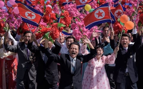 North Koreans wave flowers at Kim Jong-un as he surveys their procession from a balcony - Credit: Ed Jones/AFP