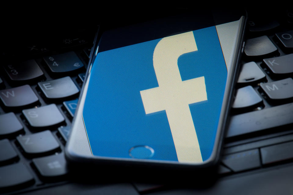 The logo of social networking site Facebook is reflected on the screen of a smartphone resting on a laptop keyboard.