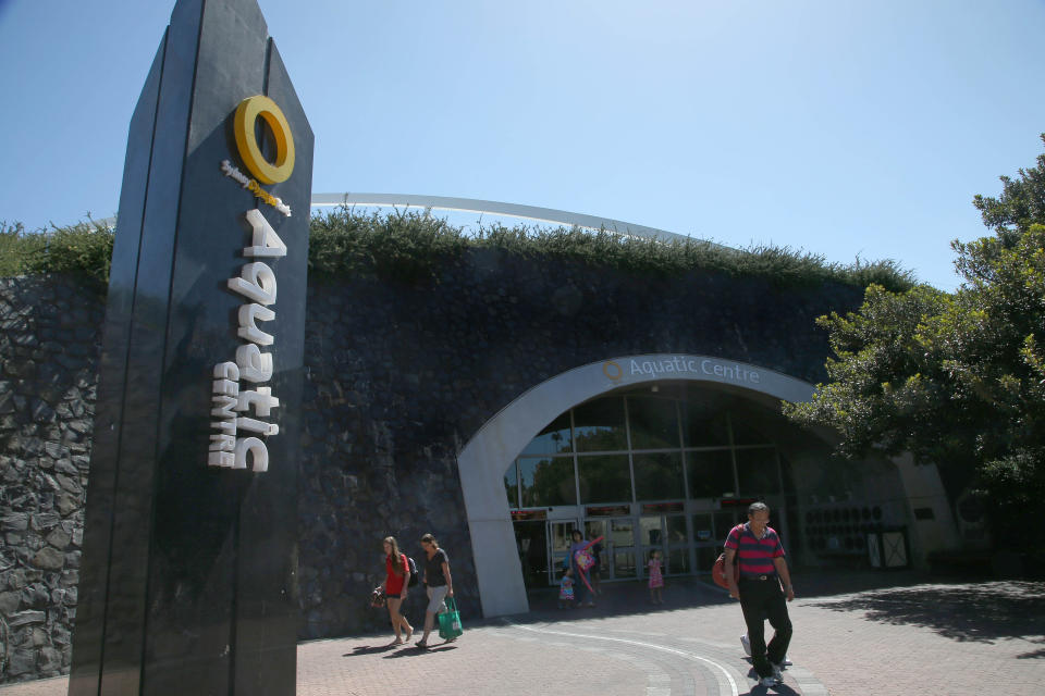 Patrons walk near the entrance of Sydney Aquatic Centre in Sydney, Monday, Feb. 24, 2014. Before the 2000 summer Olympics, the site west of Sydney where the 1580-acre Sydney Olympic Park was built was a grungy, desolate wasteland of slaughterhouses, garbage dumps and factories. Since the games, it has slowly developed into its own suburb with hotels, offices, restaurants and parklands. The park now hosts thousands of events each year, from music festivals to sports to business conferences, drawing more than 12 million annual visitors. (AP Photo/Rick Rycroft)