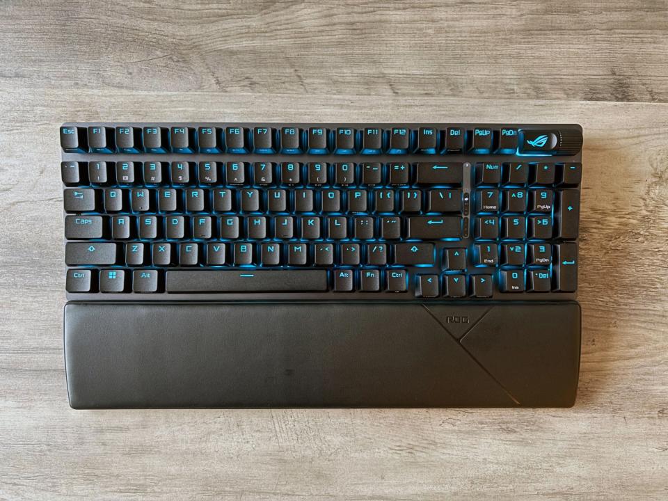 El teclado inalámbrico para juegos ASUS ROG Strix Scope II 96 descansa sobre una mesa de madera de color marrón claro.