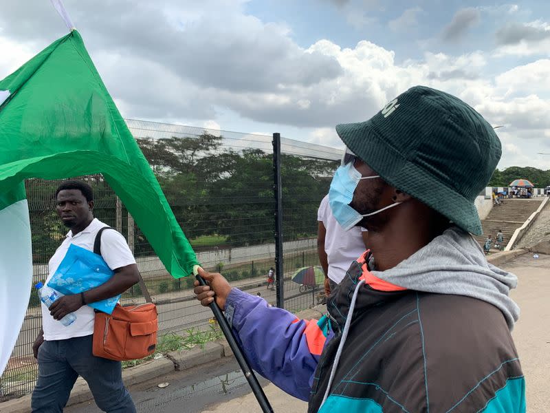 A man looks at Adebanjo Akinwunmi as he holds his flags while Nigeria marks the first anniversary of the EndSARS anti-police brutality protests in Lagos