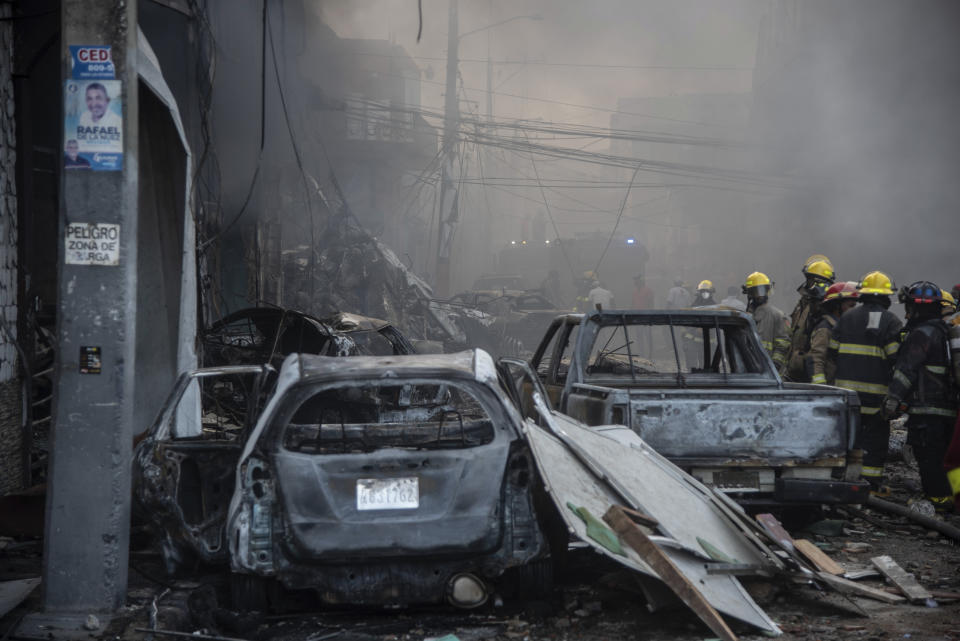 Firefighters work next to destroyed vehicles after a powerful explosion in San Cristobal, Dominican Republic, Monday, Aug 14, 2023. The Monday afternoon explosion killed at least three people and injured more than 30 others, authorities said. (Jolivel Brito/Free Daily via AP)
