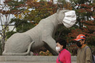 People wearing face masks to help protect against the spread of the coronavirus pass by a statue with a face mask at a park in Seoul, South Korea, Friday, Oct. 16, 2020. South Korea's daily coronavirus tally has dropped below 50 for the first time in more than two weeks despite reports of small-scale local infections. (AP Photo/Ahn Young-joon)