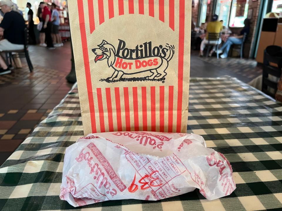 A Portillo's bag with a dog in the logo, and a sandwich in wrapping.