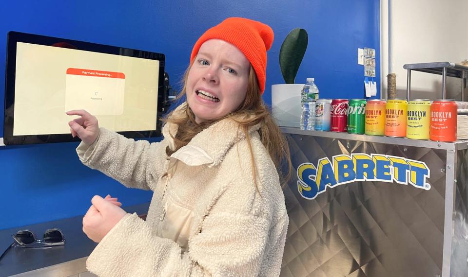 A woman using a touchscreen at a hot dog while looking distressed.