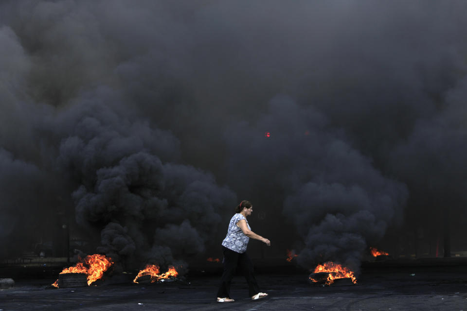 A woman walks by burning tires that were set fire to block a road during a protest against government's plans to impose new taxes in Beirut, Lebanon, Friday, Oct. 18, 2019. The protests erupted over the government's plan to impose new taxes during a severe economic crisis, with people taking their anger out on politicians they accuse of corruption and decades of mismanagement. (AP Photo/Hassan Ammar)