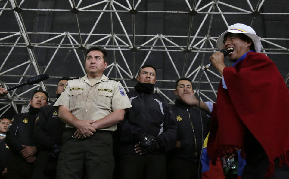 Police detained by anti-governments protesters stand on a stage as an indigenous leader speaks, in Quito, Ecuador, Thursday, Oct. 10, 2019. Thousands of protesters staged anti-government rallies Wednesday, seeking to intensify pressure on Ecuador's president after a week of unrest sparked by fuel price hikes. (AP Photo/Dolores Ochoa)