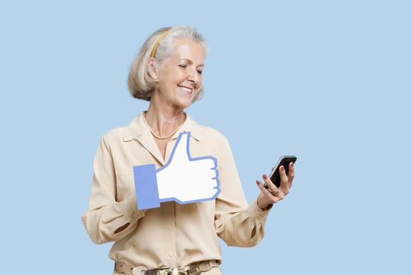 Woman looking at smartphone, with a large Facebook-like thumbs-up icon over her hand