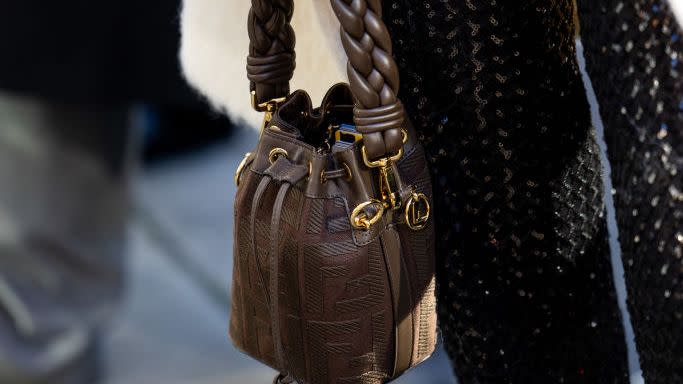 a woman carrying a brown leather fendi bucket bag with a braided handle on the street in london in a roundup of the best designer bucket bags 2024